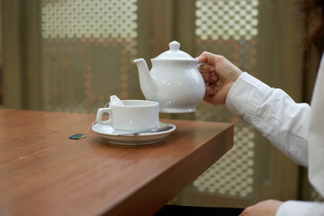 A girl pours tea into a mug while sitting at a table tea ceremony