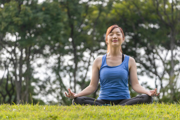 Young Asian woman in yoga suit relaxingly practicing meditation in the forest to attain happiness...
