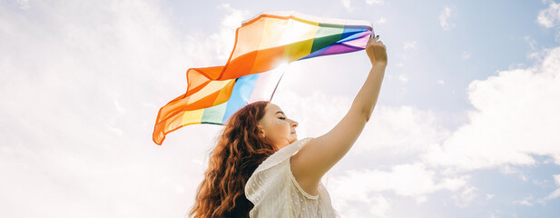 Woman with rainbow flag on sky background.