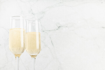 Festive background with sparkling champagne in two glasses on white soft light  marble backdrop, closeup, top part. Holiday drink for celebration event, copy space.