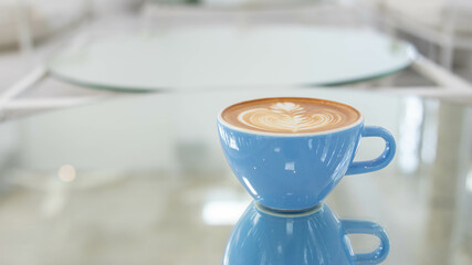 blue cup of art latte on a table in a cafe. Foam flower on top of the cup.Little spoon and plate.Close up coffee cup on table.