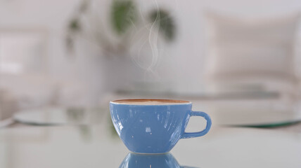 blue cup of art latte on a table in a cafe. Foam flower on top of the cup.Little spoon and plate.Close up coffee cup on table.