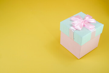 Pink and cyan gift box with ribbon bow isolated on yellow background