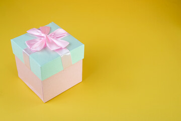 Pink and cyan gift box with ribbon bow isolated on yellow background