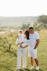 Young family with cute little daughter walking in forest on the sunset