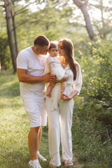 Fototapeta premium Young family with cute little daughter walking in forest on the sunset