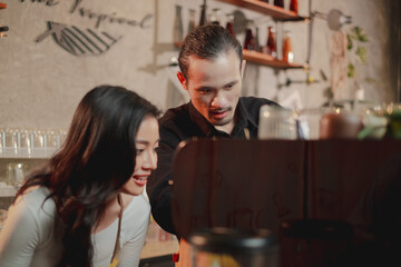 A male barista or owner is teaching, training, coaching or showing a trainee or new staff how to make a coffee at coffee shop and cafe. Concept of upgrading skill of worker, preparing a coffee.