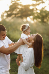 Fototapeta premium Young family with cute little daughter walking in forest on the sunset