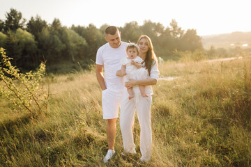 Fototapeta premium Young family with cute little daughter walking in forest on the sunset