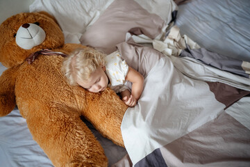 Children's daytime sleep. The child sleeps next to a large teddy bear.