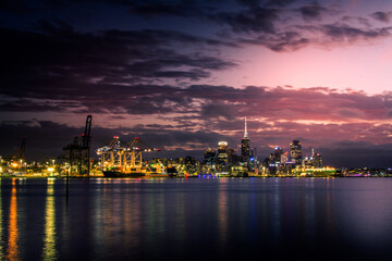 Fototapeta na wymiar Bright lights of Auckland downtown at sunset. Dramatic view over Auckland City from North Shore