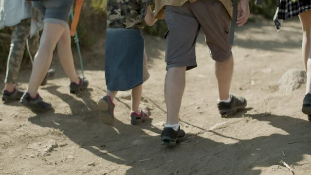 Legs closeup of hiking family walking along dirt road together. Caucasian family travelling on foot, enjoying outdoor leisure activity. Back view. Travel, family, holiday concept.