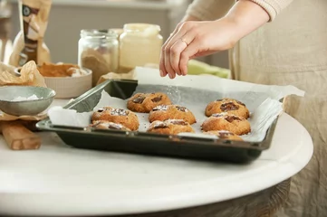 Foto op Canvas Closeup of female hands putting cookies on the black baking sheet pouring on ingredients around © Simone Oppes/Wirestock Creators