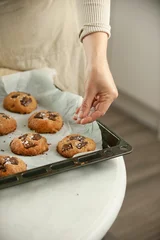 Tuinposter Vertical closeup of female hands putting cookies on the black baking sheet ingredients around © Simone Oppes/Wirestock Creators