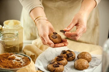 Tuinposter Closeup of female hands putting cookies on the black baking sheet pouring on ingredients around © Simone Oppes/Wirestock Creators