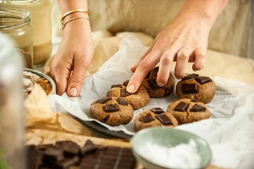 Tuinposter Closeup of female hands putting cookies on the black baking sheet pouring on ingredients around © Simone Oppes/Wirestock Creators