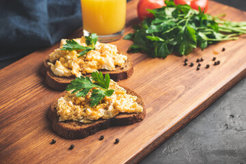 Scrambled eggs with parsley on bread, homemade healthy breakfast on dark wooden board