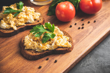 Scrambled eggs with parsley on bread, homemade healthy breakfast on dark wooden board