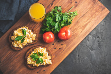Scrambled eggs with parsley on bread, homemade healthy breakfast on dark wooden board, top view