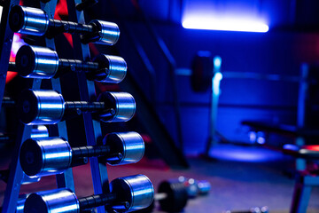 Rack with a set of metal silvery dumbbells in the gym. Shiny dumbbells of different weights and...