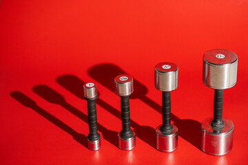 Set of metal silvery dumbbells on a red background with falling shadows. Four dumbbells of...