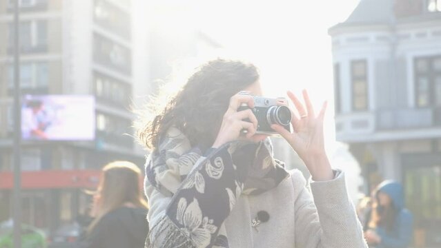 Curly hair woman photographer taking photos with a vintage film camera on the city streets