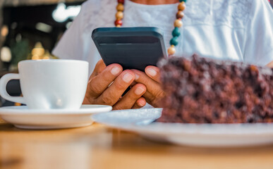 Woman hands holding smartphone while relaxing for a break at coffee shop with chocolate cake and coffee cup.