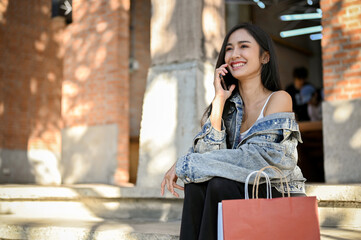 Attractive Asian female with her shopping bags, talking on the phone while sitting on the street stairs.