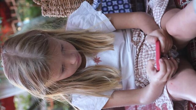 Cute little girl sits in an unhealthy position and uses a mobile phone. Harm to health from electronic device