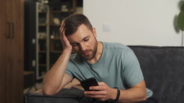 An upset man tries to distract himself from his thoughts with the help of a smartphone, but it doesn't work, depression takes over the young man
