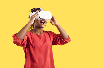 Smiling African American woman enjoy vision in vr glasses isolated on yellow studio background. Happy excited black wear virtual reality headset explore new horizons. Technology concept.