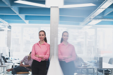 Portrait of young smiling business woman in creative open space coworking startup office. Successful businesswoman standing in office with copyspace. Coworkers working in background.