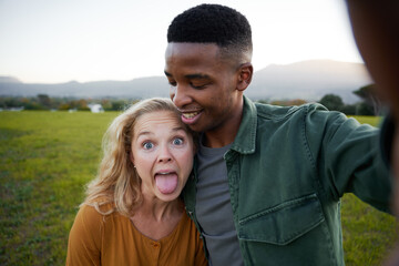 Young multiracial couple in casual clothing smiling and sticking out tongue in field