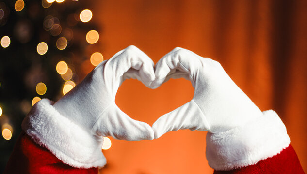 Santa Claus making the heart shape with hand against the tree in Christmas