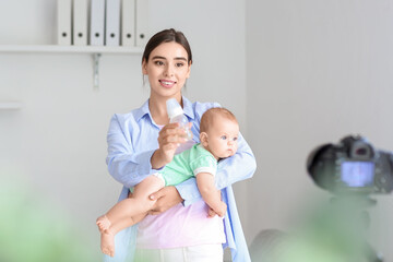 Young woman with baby and bottle recording video course at home