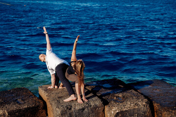 Lover Couple man and woman are doing yoga against background sea and blue sky