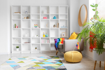 Interior of modern living room with shelving unit, armchair, houseplants and rainbow flags