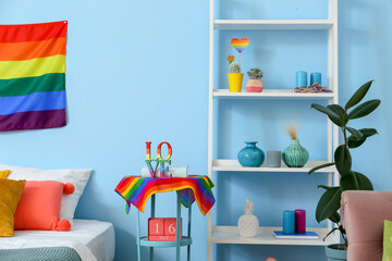 Stylish shelving unit and table with rainbow flags near blue wall