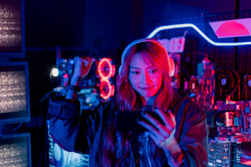 Winning or You Win. Young woman gamer champion excited, Happy gamer people playing video game online with smart mobile phone with neon lights raises hands to wins celebrating, game and e-sports.