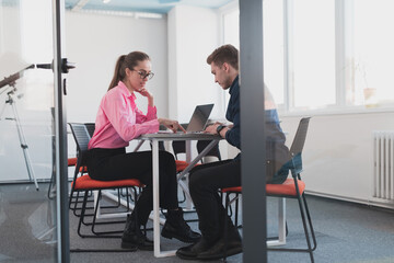 Two young entrepreneurs, a businessman and a businesswoman, sitting in a modern glass office and exchange business ideas