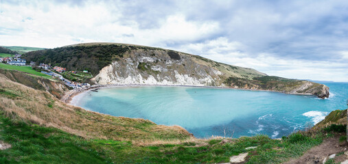 Fototapeta na wymiar Panoramic views of Lulworth Cove in Dorset, United Kingdom. Part of Jurassic Coast World Heritage Site, view of stone cliffs and blue sea, selective focus
