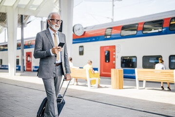 Smiling entrepreneur holding smart phone while walking at train station platform