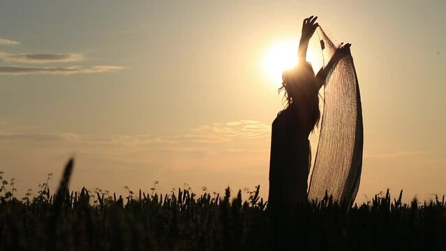 backlight of a dreamy woman dancing with a veil illuminated by the heat of the sun