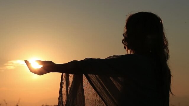 silhouette of a woman at sunset looking after the sun in her hands