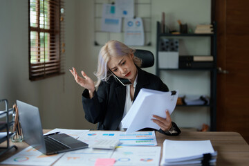 Portrait of a young Asian woman showing a serious face as she uses her phone, financial documents...