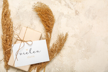 Card with text VIELEN DANK, gift box and pampas grass on grunge background