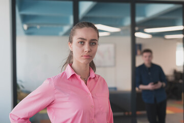 Obraz premium Portrait of young smiling business woman in creative open space coworking startup office. Successful businesswoman standing in office with copyspace. Coworkers working in background.