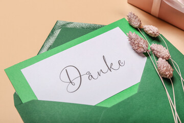 Card with word DANKE, envelope and pampas grass on beige background, closeup