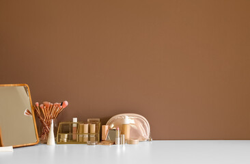 Different cosmetics and makeup brushes on table near color wall