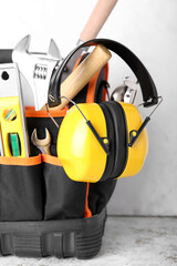 Bag with builder's tools and hearing protectors on light background
